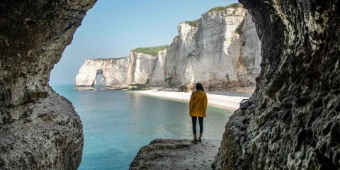Falaises d’Étretat vues depuis une grotte avec randonneur face à la mer en Normandie