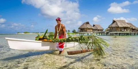 Accueil en pirogue fleurie devant des bungalows sur pilotis en Polynésie française