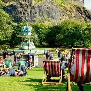 Des visiteurs se détendent près de la Ross Fountain dans les Princes Street Gardens à Édimbourg, avec le château en arrière-plan.