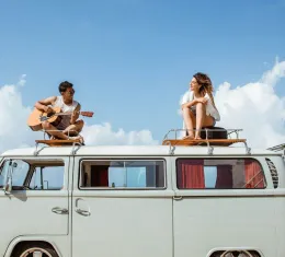 Jeune homme chantant avec une guitare sur le toit d’un van vintage, avec une amie.