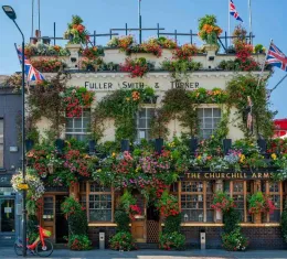 Façade du pub Churchill Arms à Londres couverte de fleurs colorées avec drapeaux britanniques