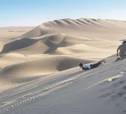 es voyageurs descendent les dunes du Cerro Blanco en sandboard dans le désert de Sechura, au Pérou.