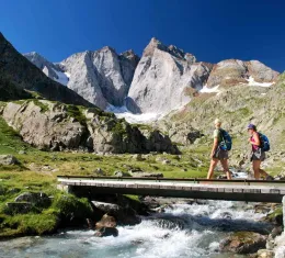 Deux randonneurs franchissent une passerelle face au massif du Vignemale dans les Pyrénées