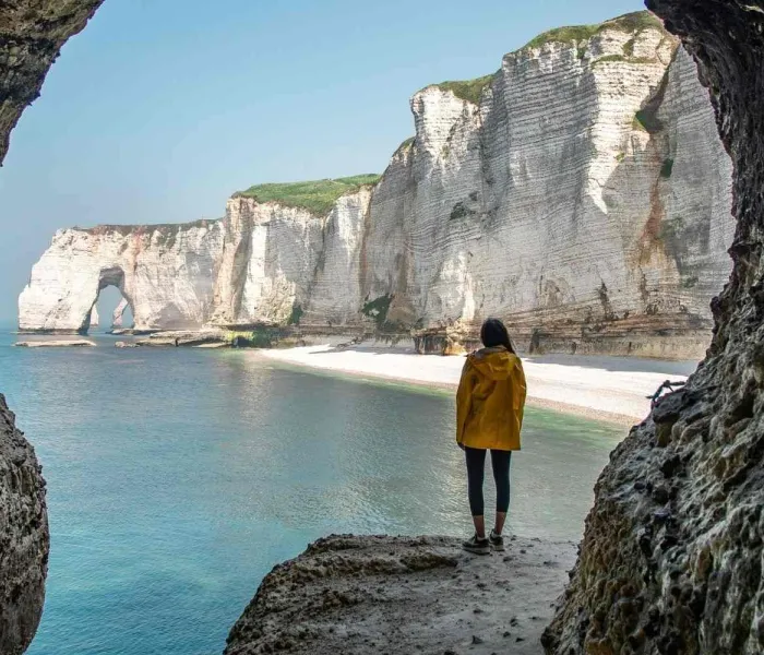 Falaises d’Étretat vues depuis une grotte avec randonneur face à la mer en Normandie
