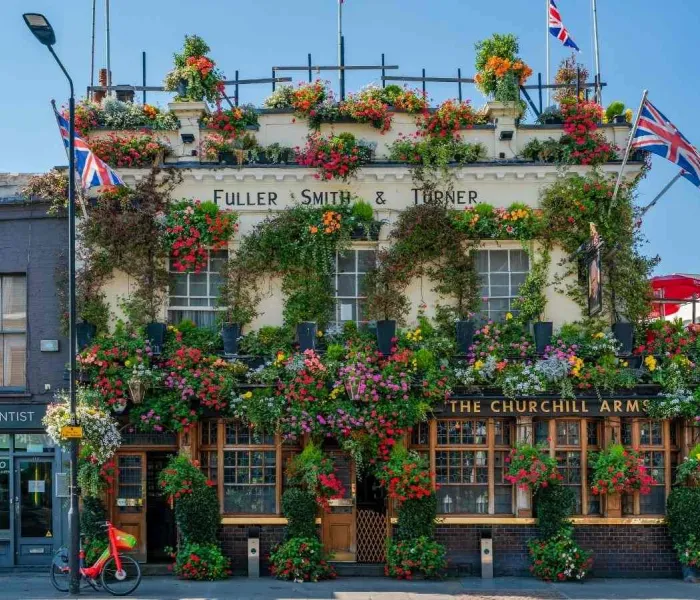 Façade du pub Churchill Arms à Londres couverte de fleurs colorées avec drapeaux britanniques
