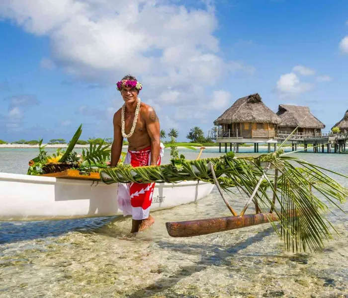 Accueil en pirogue fleurie devant des bungalows sur pilotis en Polynésie française