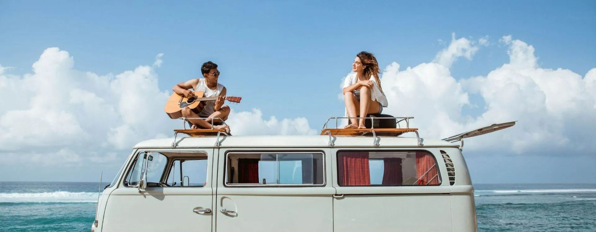 Jeune homme chantant avec une guitare sur le toit d’un van vintage, avec une amie.