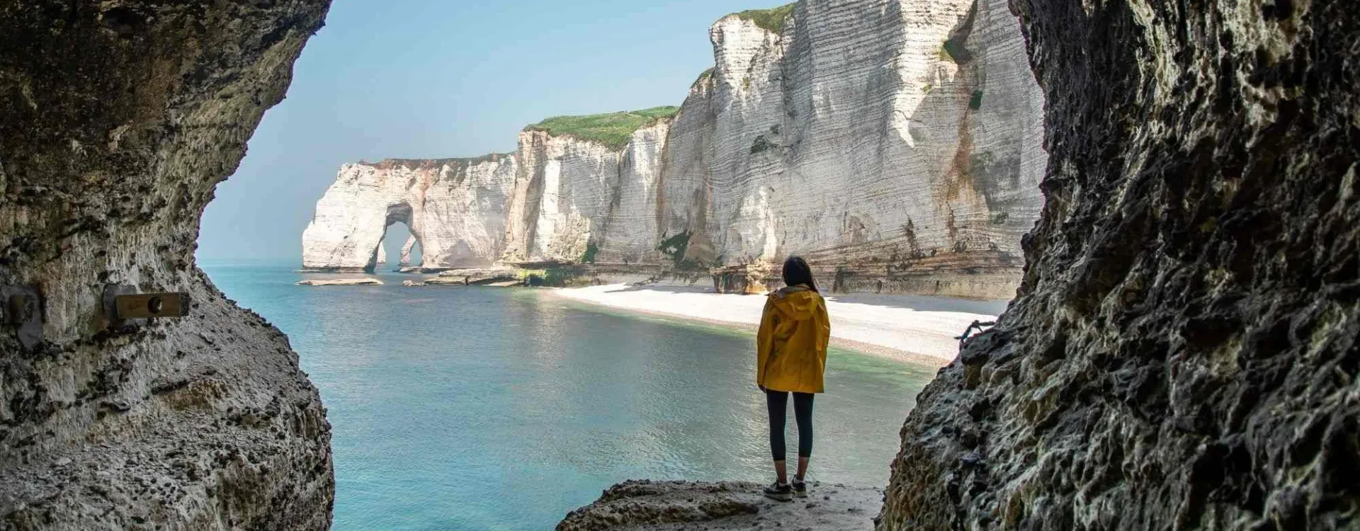Falaises d’Étretat vues depuis une grotte avec randonneur face à la mer en Normandie