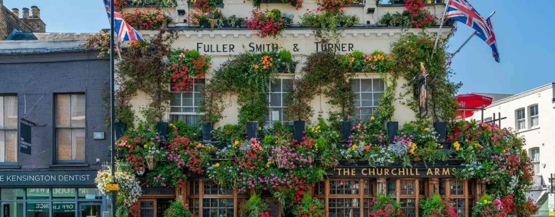 Façade du pub Churchill Arms à Londres couverte de fleurs colorées avec drapeaux britanniques