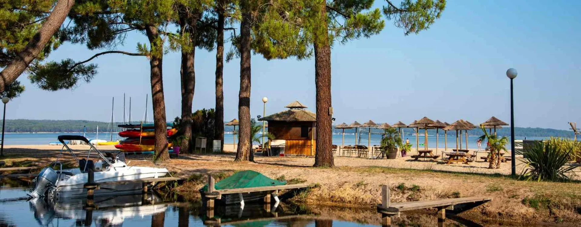 Plage aménagée au bord d'un lac de Biscarrosse dans les Landes, avec pins maritimes, bateaux et activités nautiques