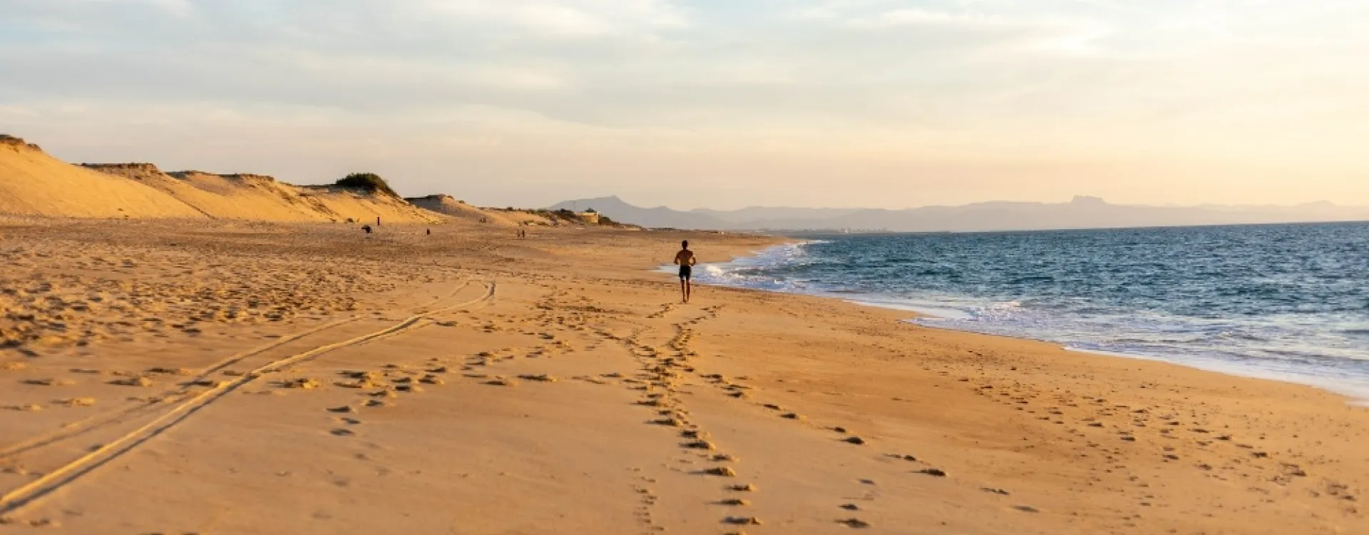 Une personne marche sur une plage sauvage des Landes bordée par les dunes et l'océan Atlantique