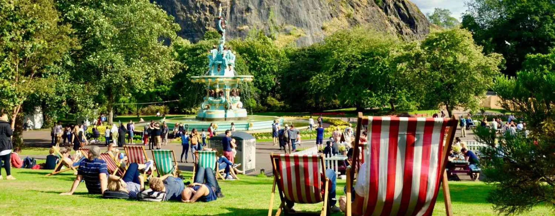 Des visiteurs se détendent près de la Ross Fountain dans les Princes Street Gardens à Édimbourg, avec le château en arrière-plan.