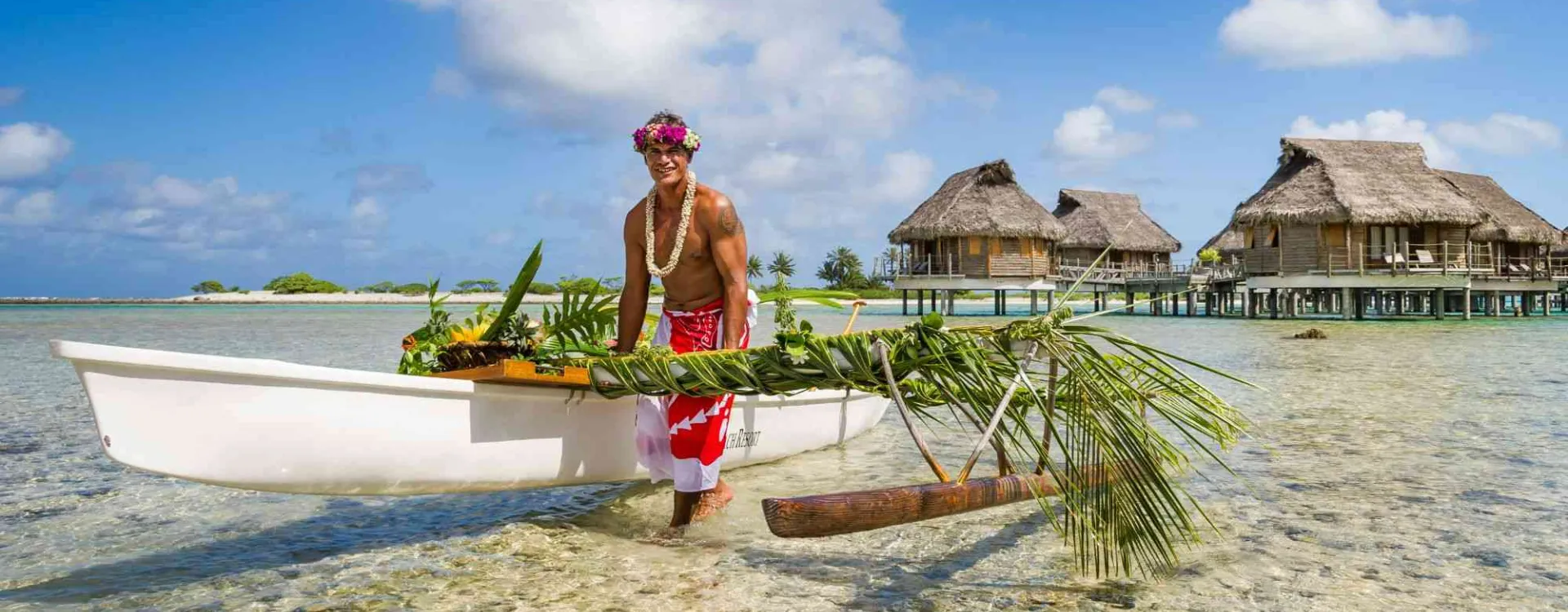 Accueil en pirogue fleurie devant des bungalows sur pilotis en Polynésie française