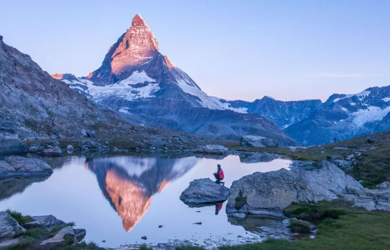 Randonneur agenouillé près d’un lac face au Cervin au lever du soleil