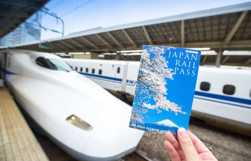 Japan Rail Pass tenu en main devant un Shinkansen à Tokyo Station, solution économique pour voyager en train au Japon
