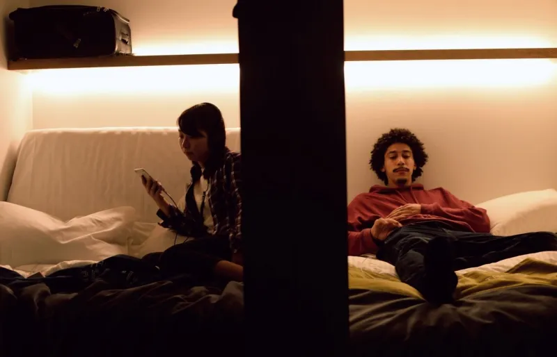 Voyageurs assis dans des capsules adjacentes dans un hôtel capsule au Japon, hébergement économique pour un séjour à petit budget