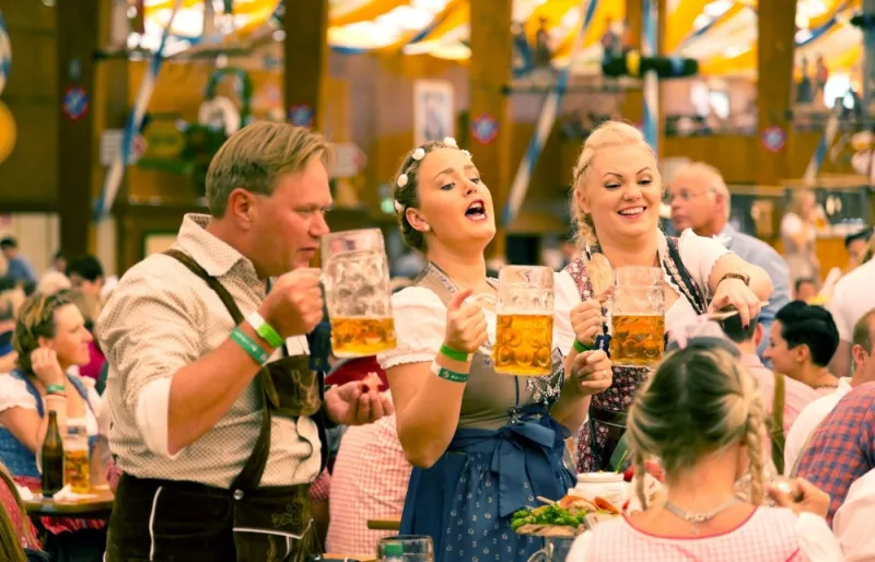 Un groupe de jeunes en costumes traditionnels bavarois trinquant avec des chopes de bière lors de l’Oktoberfest à Munich
