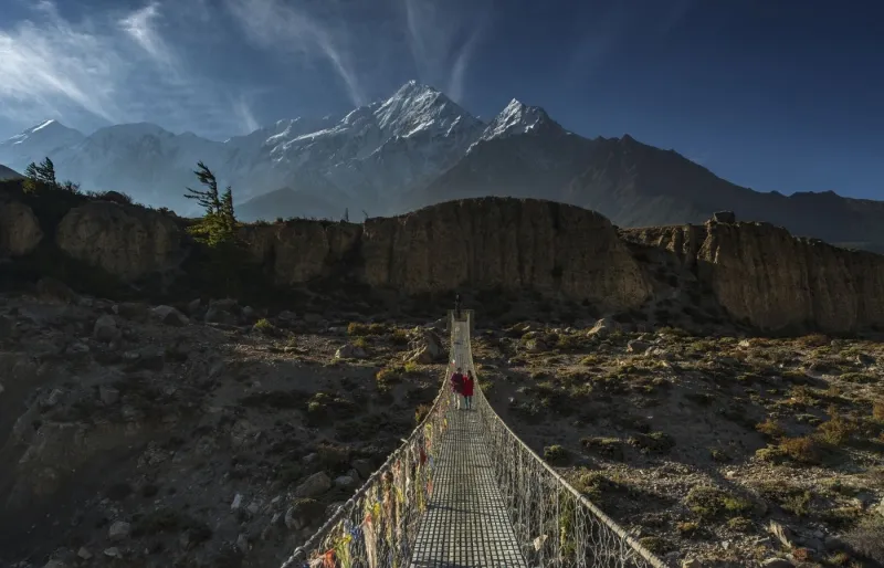 Randonneurs traversant un pont dans la vallée de la Kali Gandaki face aux montagnes Nilgiri sur le trek de Jomsom dans la région de l’Annapurna au Népal