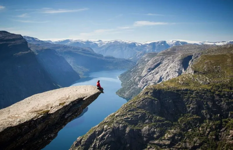 Randonneur assis sur la falaise de Trolltunga au-dessus d’un fjord en Norvège