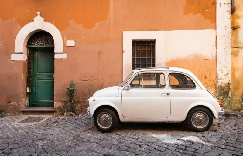 Voiture vintage garée dans une rue du quartier de Trastevere à Rome, symbole d’un road trip en Italie.