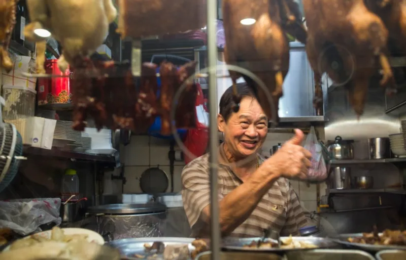 Stand de street food au Newton Hawker Centre à Singapour avec canards laqués suspendus et chef souriant