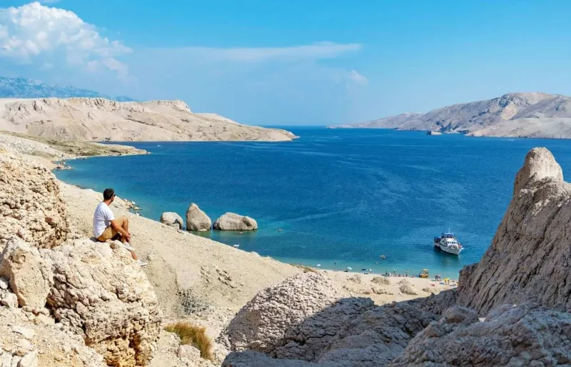 Personne assise sur une falaise au-dessus de la plage de Beritnica sur l’île de Pag en Croatie