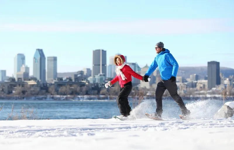 Couple en raquettes dans la neige à Montréal avec skyline en arrière-plan par grand froid