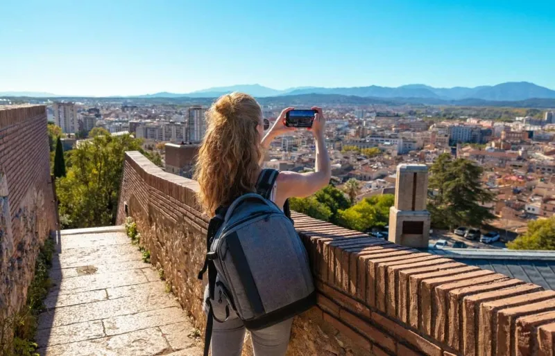 Vue panoramique sur Gérone depuis les remparts avec une touriste prenant une photo