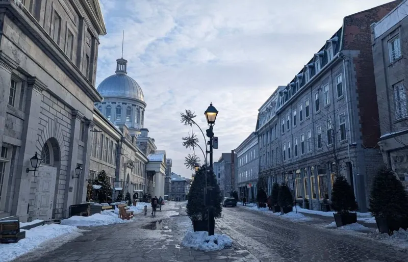 Rue pavée du Vieux-Montréal enneigée avec vue sur le dôme du marché Bonsecours en hiver
