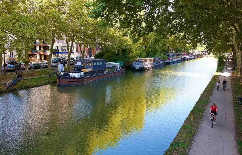 Cyclistes le long du Canal du Midi à Toulouse sur le chemin de halage bordé de péniches et de platanes