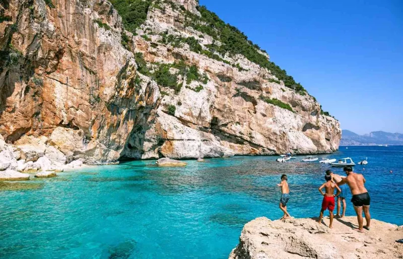 Enfants sautant dans les eaux turquoise de Cala Mariolu pendant des vacances en famille en Sardaigne