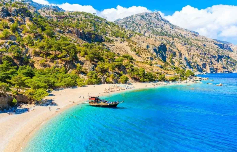 La plage d’Apella à Karpathos dans le Dodécanèse avec eau turquoise, montagnes rocheuses et bateau