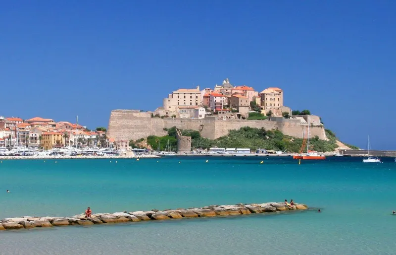 La plage de Calvi en Corse avec la citadelle en arrière-plan et ses eaux turquoise