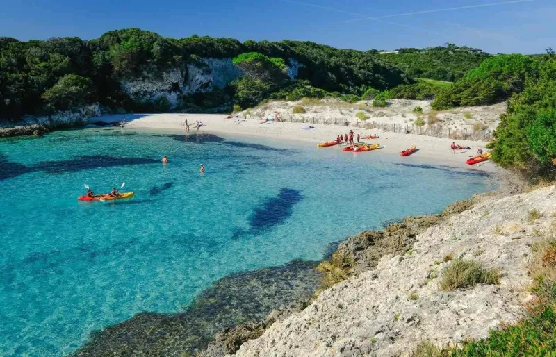 La plage du Petit Spérone en Corse-du-Sud, avec son eau turquoise cristalline et des kayakistes dans la baie.