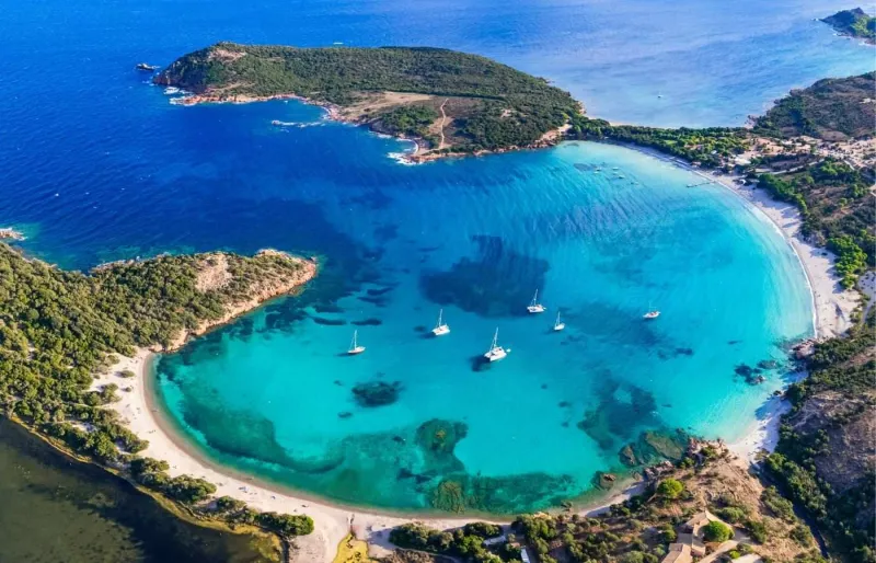 Vue aérienne de la plage de Rondinara en Corse, baie en forme de coquille avec sable clair et eaux turquoise.