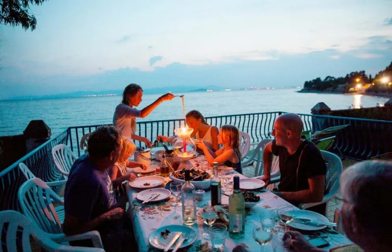 Famille avec enfants en train de dîner en terrasse au bord de la mer pendant des vacances en Sardaigne