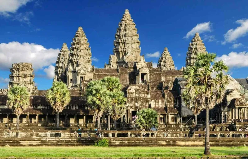 Vue du temple d'Angkor Vat au Cambodge avec ses tours emblématiques et ses palmiers sous un ciel bleu