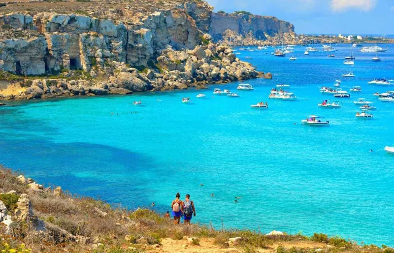 Randonneurs descendant vers Cala Rossa à Favignana avec ses eaux turquoise et ses falaises rocheuses