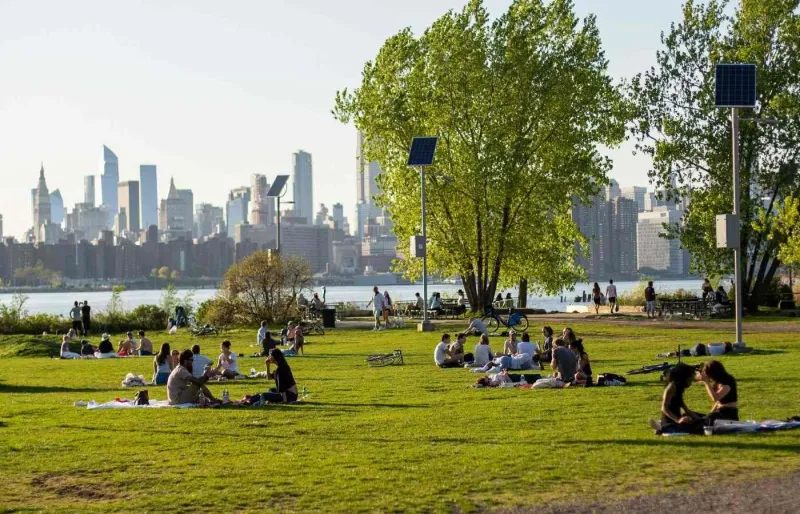 Visiteurs profitant des pelouses de Domino Park avec vue sur la skyline de Manhattan depuis Williamsburg à Brooklyn