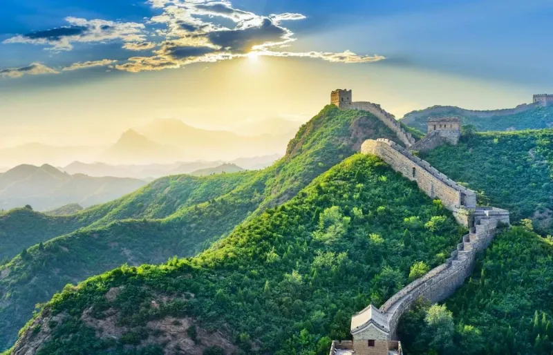 Vue panoramique de la Grande Muraille de Chine serpentant à travers les montagnes verdoyantes au coucher du soleil
