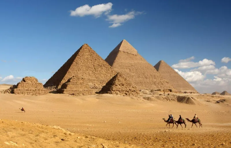 Vue des pyramides de Gizeh en Égypte avec des chameaux traversant le désert au premier plan