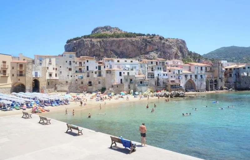 Plage de Cefalù bordée par les maisons du centre historique avec la Rocca en arrière-plan en Sicile