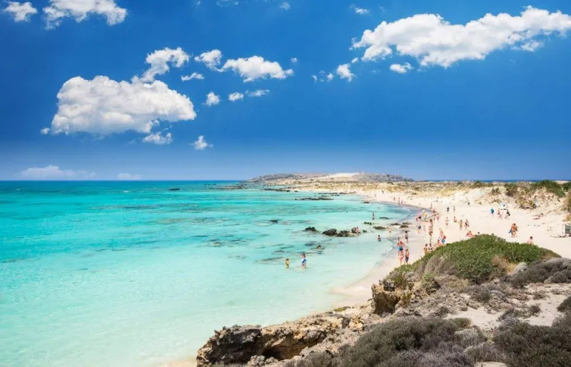 Vue panoramique de la plage d'Elafonissi en Crète avec son lagon aux eaux turquoise et son sable clair bordé de dunes.