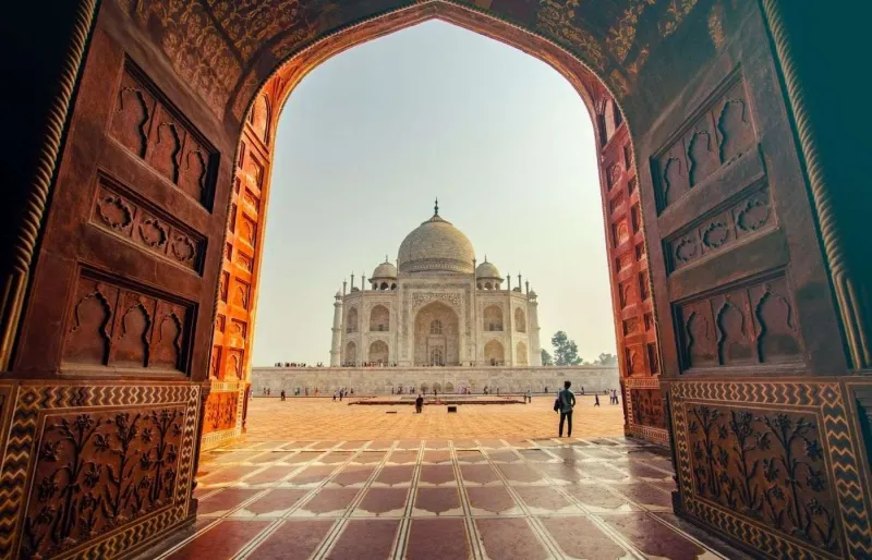 Vue du Taj Mahal à Agra encadré par une arche monumentale avec sa façade en marbre blanc