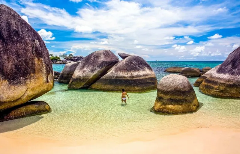Personne marchant dans les eaux cristallines de Tanjung Tinggi Beach parmi les célèbres rochers de granite de Belitung