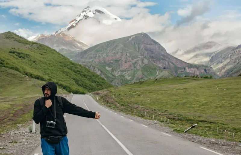 Auto-stoppeur portant un coupe-vent et un sac à dos sur une route de montagne