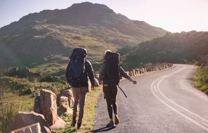 Deux voyageurs font de l'auto-stop en pleine journée sur une route de montagne.