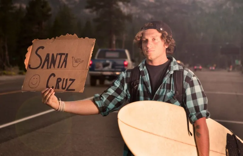Auto-stoppeur tenant une pancarte indiquant sa destination "Santa Cruz" pour trouver un trajet en auto-stop.