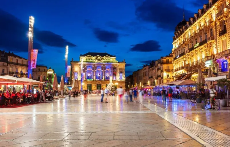 Place de la Comédie illuminée de nuit et ses terrasses animées à Montpellier.