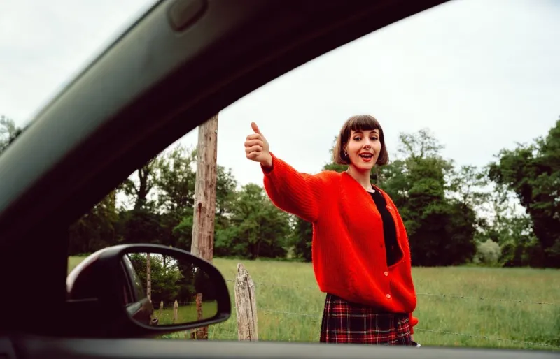 Voyageuse souriante faisant de l'auto-stop avec le pouce levé au bord de la route.